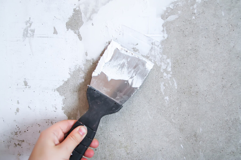 A putty knife scraping plaster onto a wall.