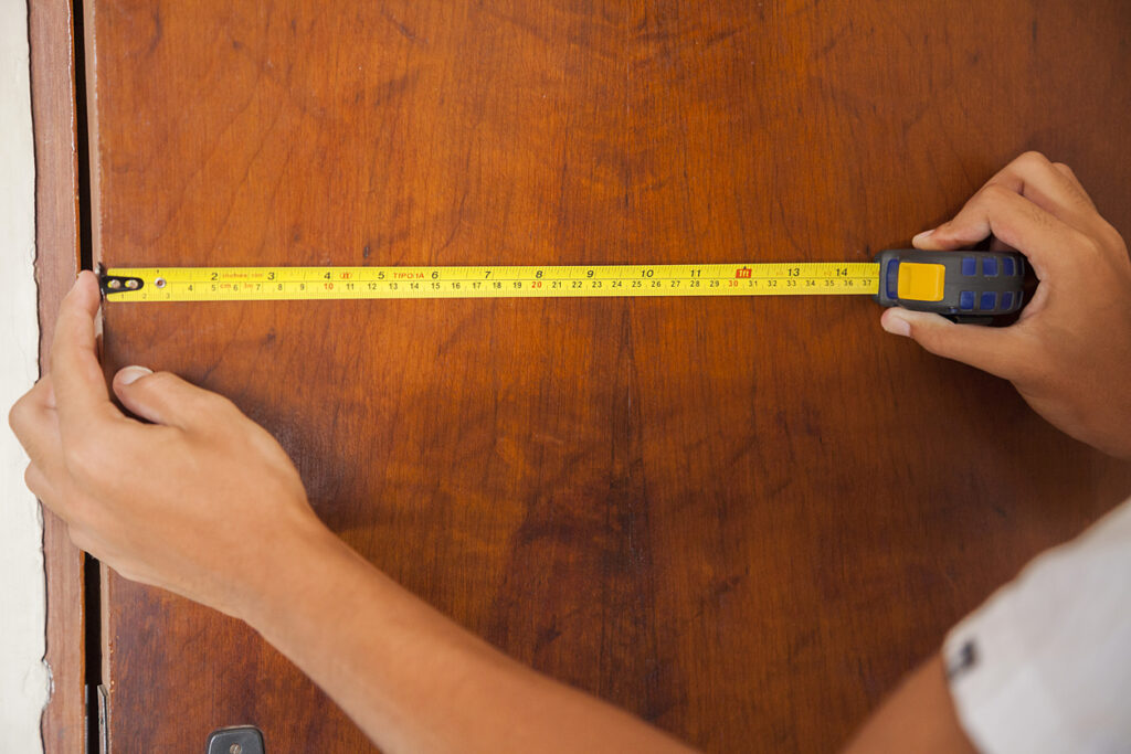 A person using a measuring tape to measure the width of a door