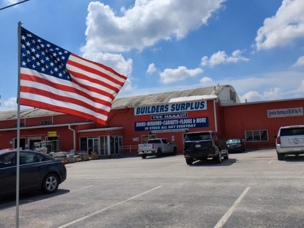 A storefront of a building surplus store with an American flag in the foreground.