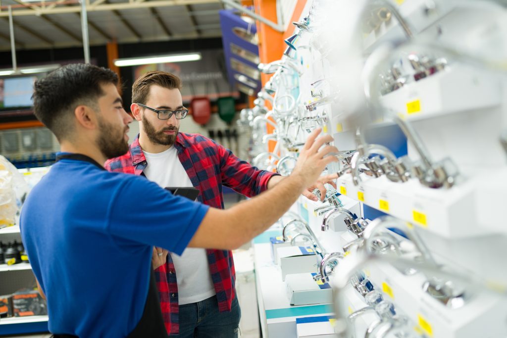 Rear view of a male employee and a customer talking and looking for a new bathroom faucet while shopping at the hardware store