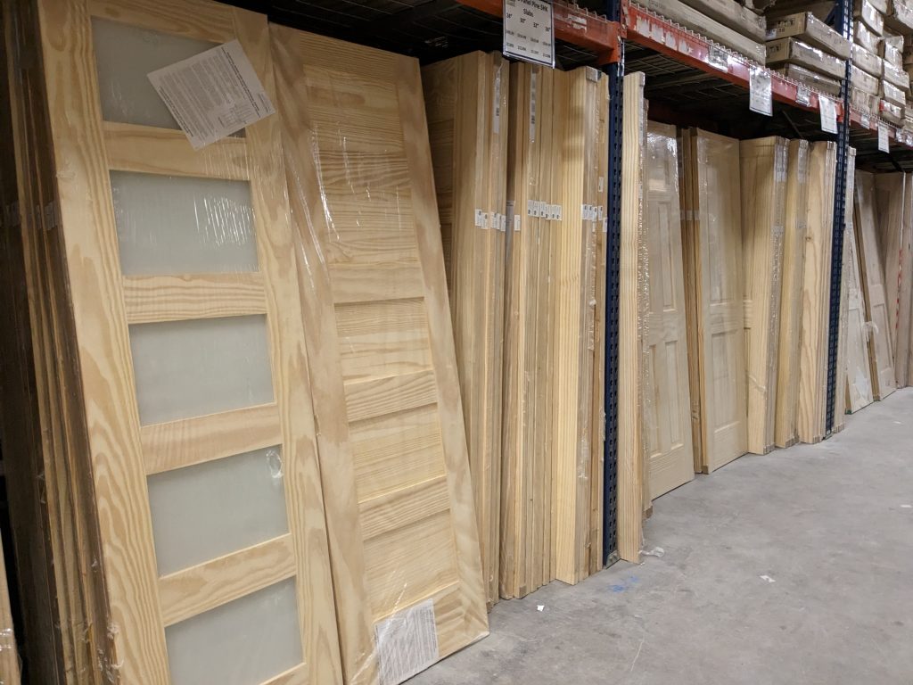 Bays of interior pine doors in warehouse racking. Piles of pine doors with glass and panel pine doors leaning in between racking.