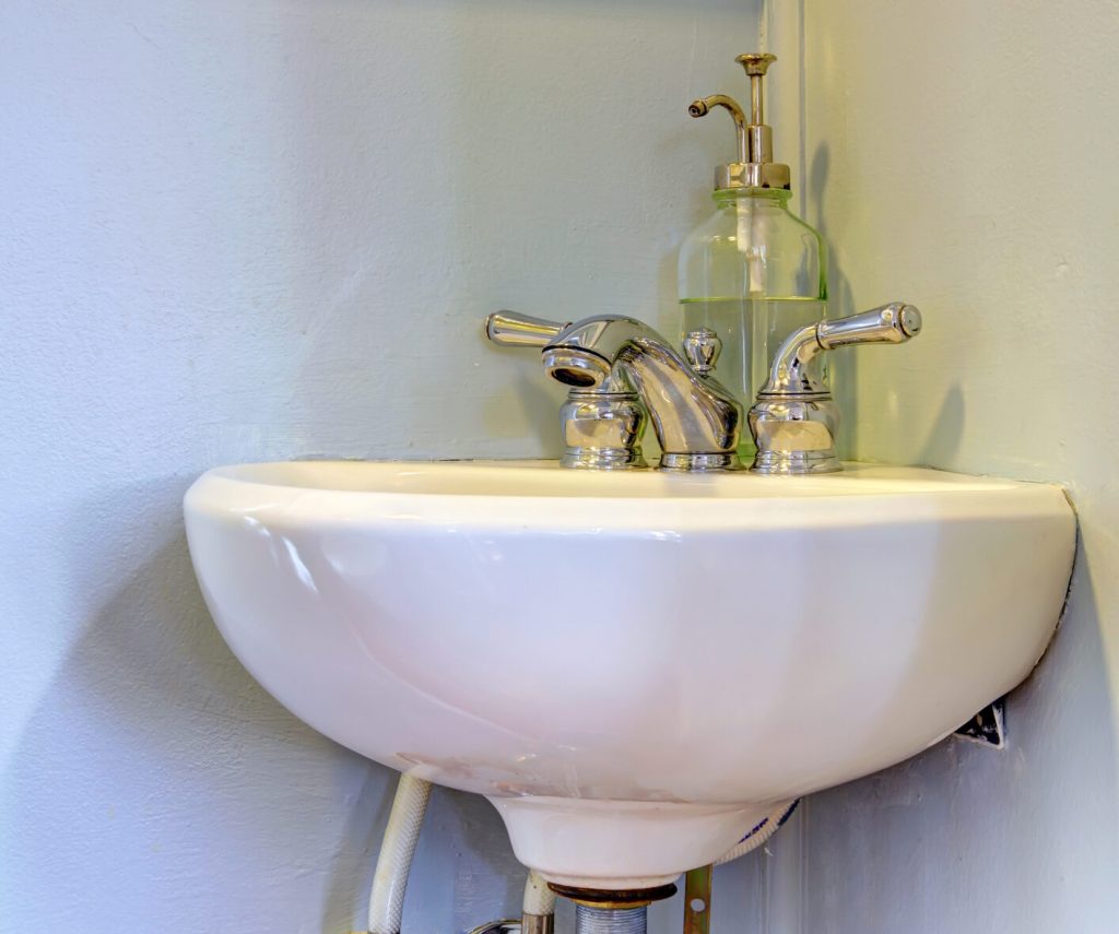 Small corner sink with grey wall and soap.