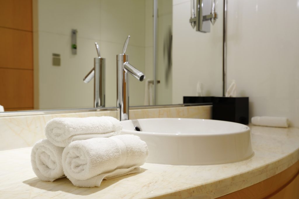 Interior of modern bathroom with drop in sink, shower cubicle, big mirror, white bath towel and toilet.